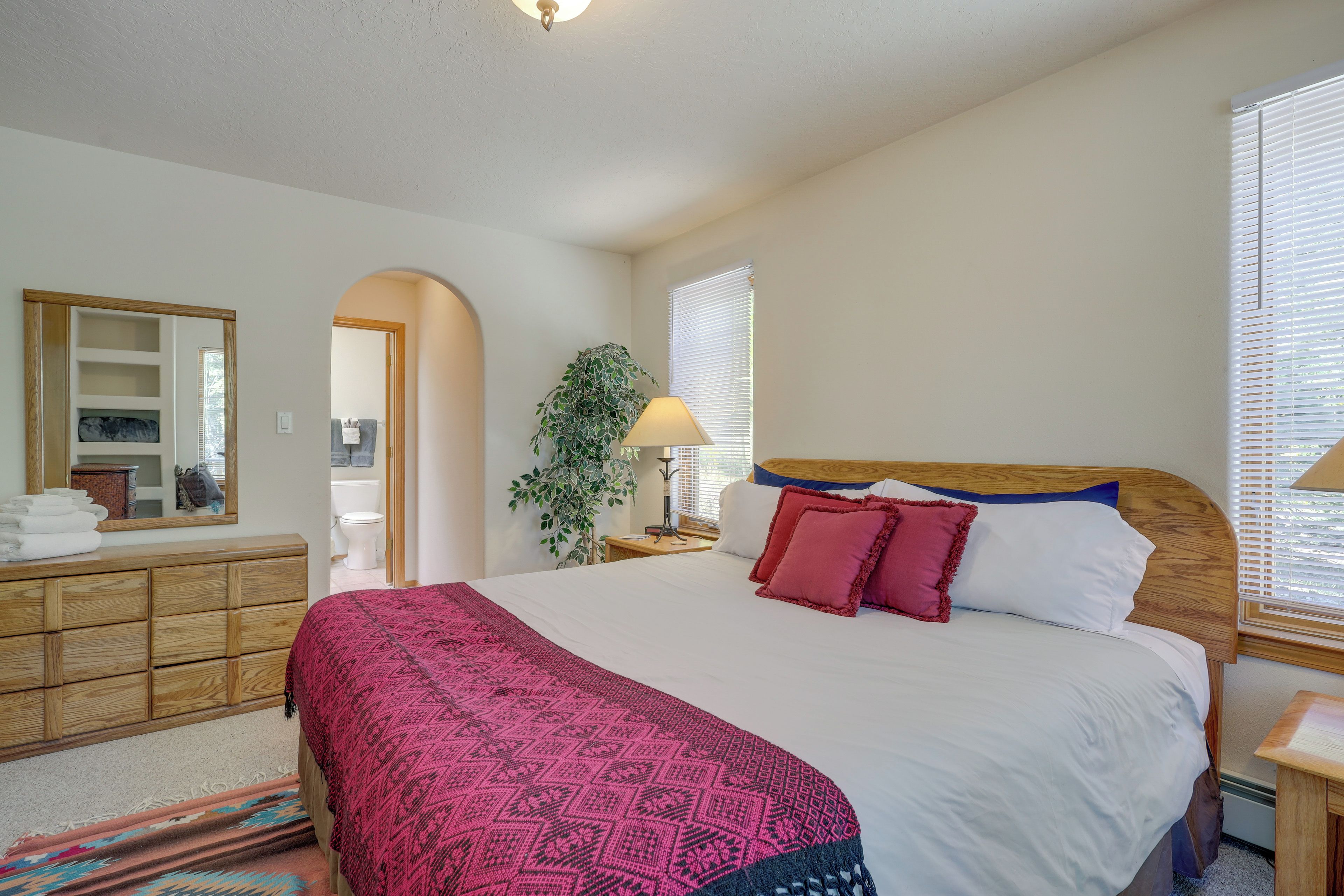A bedroom with a large bed, wooden dresser, and a mirror.
