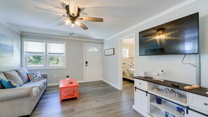 A modern living room with a ceiling fan, a flat-screen TV, a sofa with colorful cushions, and a small orange table. - New Bern Vacation Rental: Close to Neuse River! (New Bern)