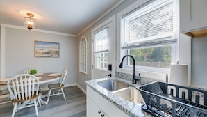 A kitchen with white cabinetry, a granite countertop, a double sink, and a dining area with white chairs and a table. - New Bern Vacation Rental: Close to Neuse River! (New Bern)