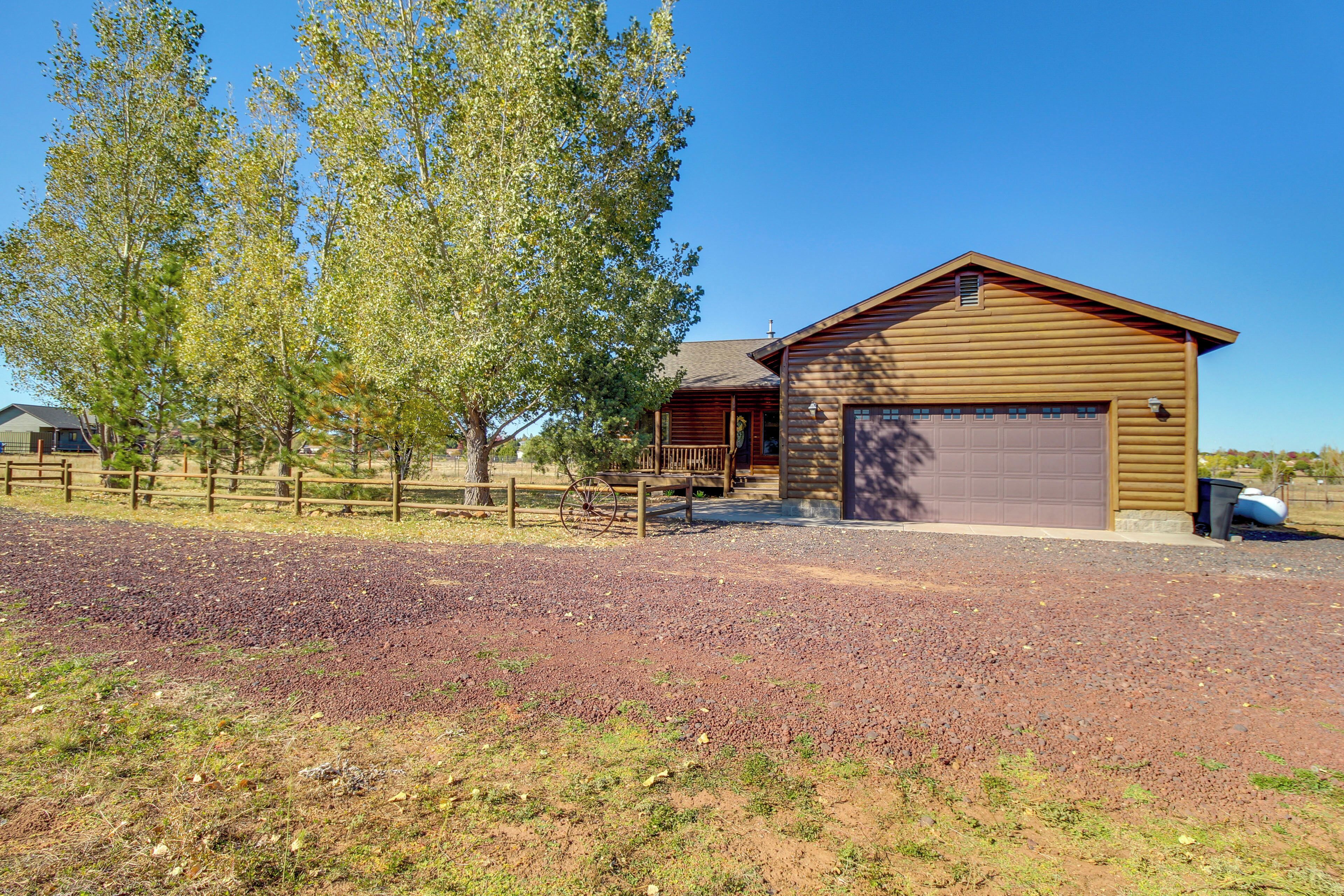 A wooden barn with a garage, surrounded by a gravel driveway and a wooden fence.