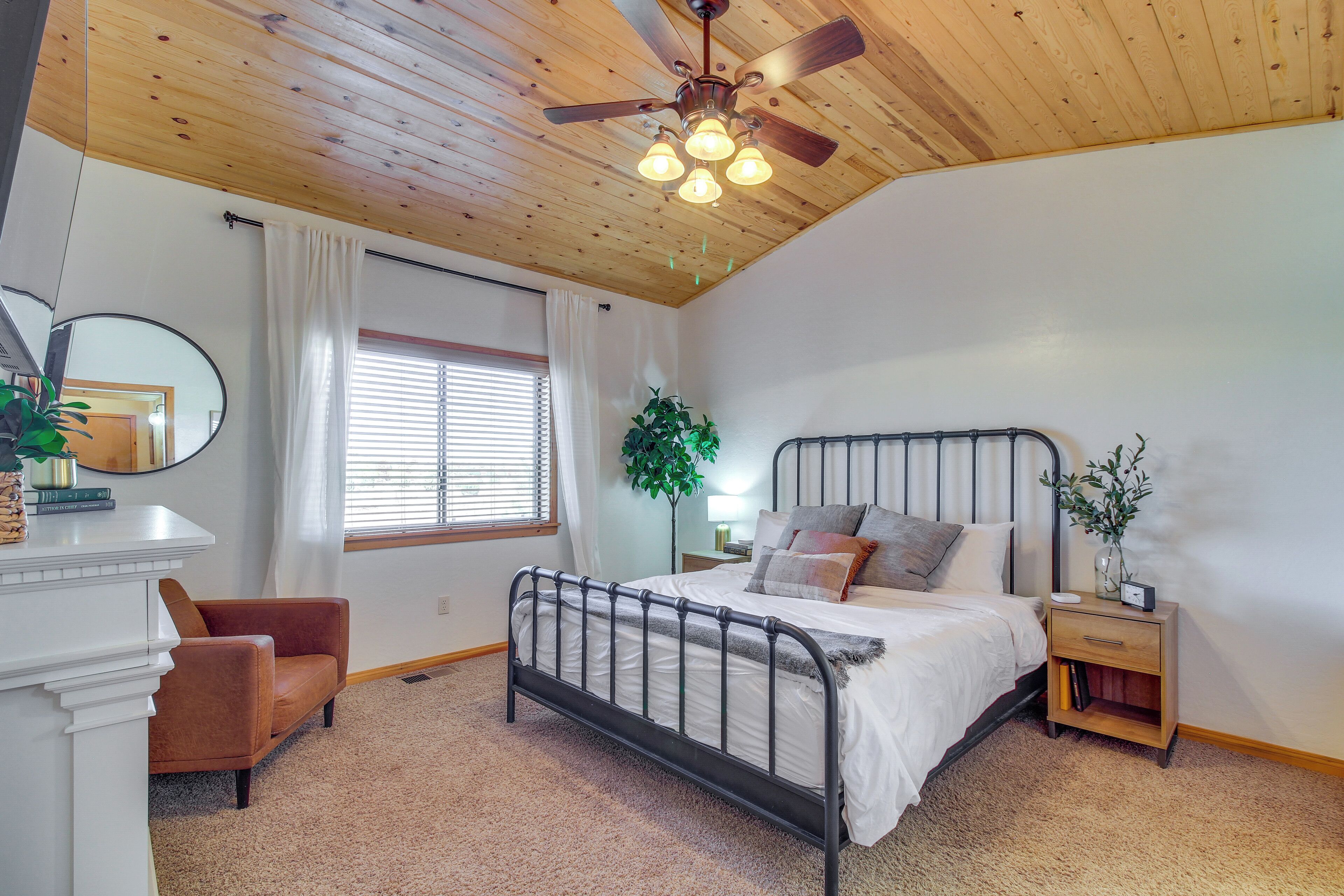 A bedroom with a bed, a nightstand, a chair, a ceiling fan, and a window with curtains.