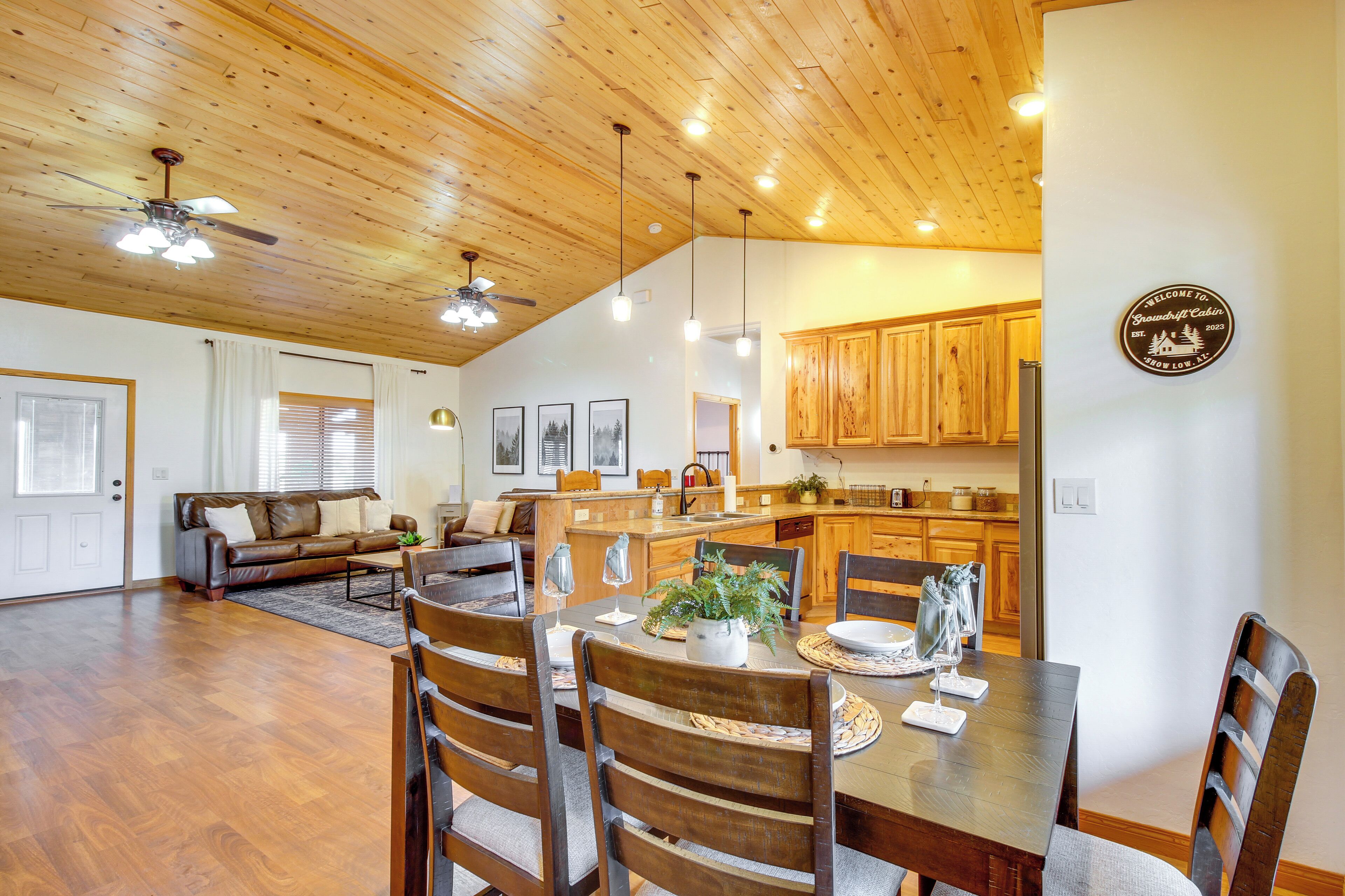 Amplia sala de estar con techo de madera, una mesa de comedor con sillas y una cocina con armarios de madera.
