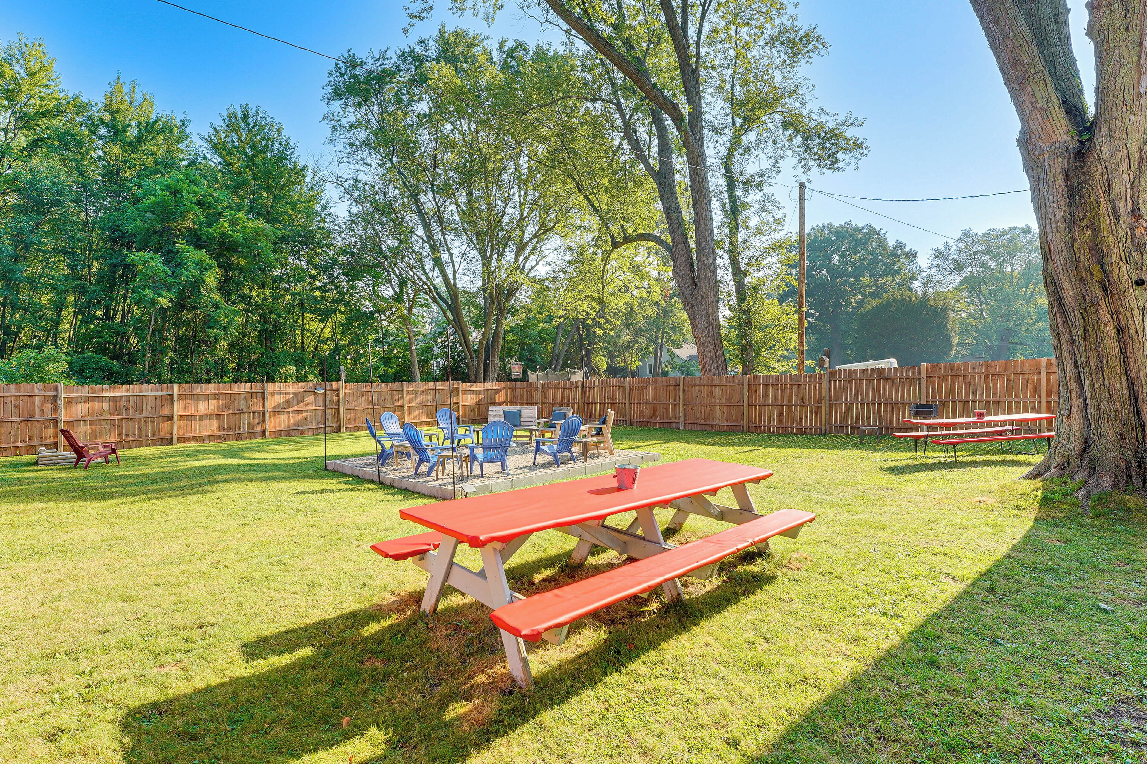 A backyard with a picnic table and chairs, surrounded by a wooden fence and trees.
