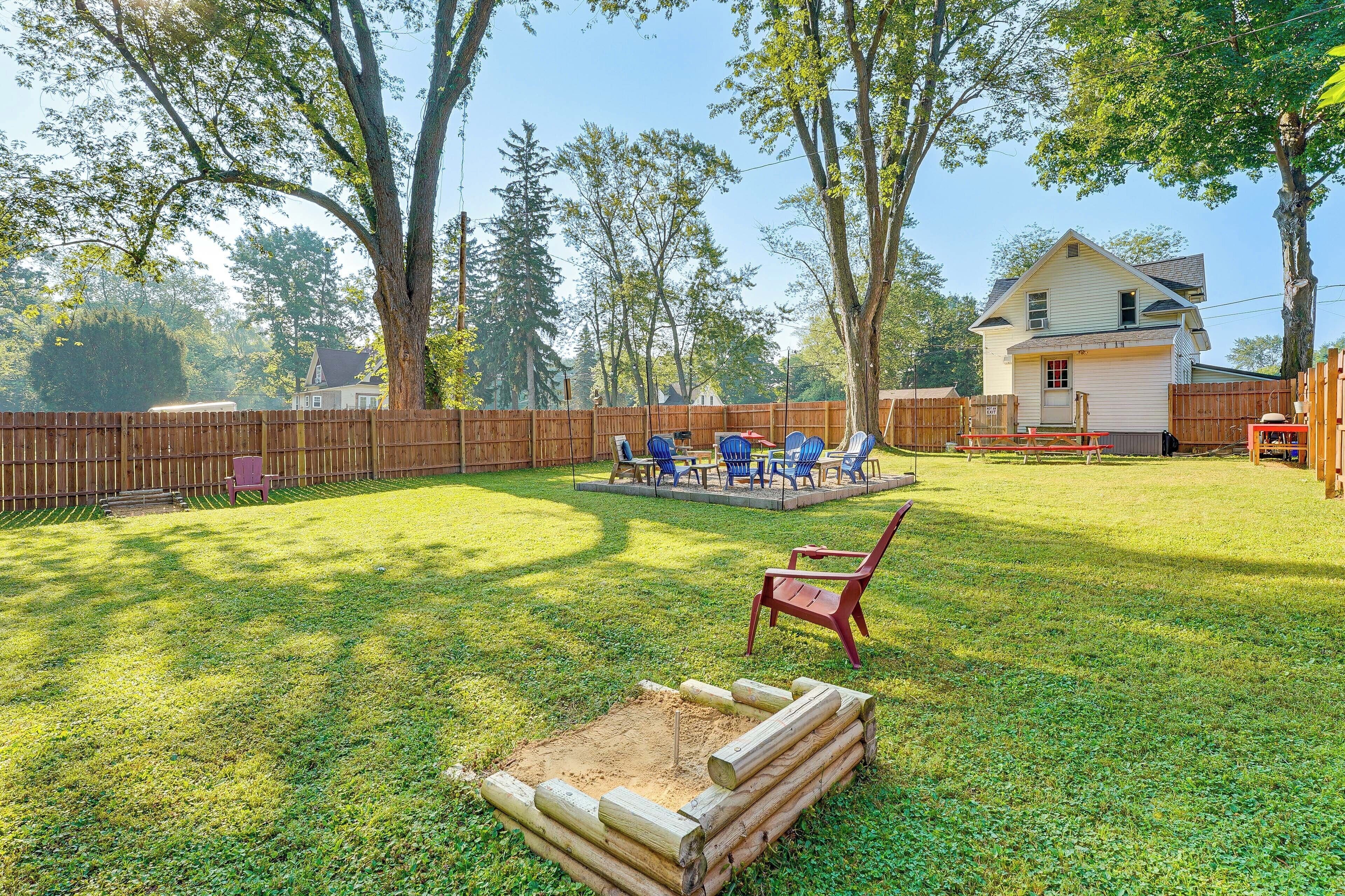 A backyard with a wooden fire pit, a patio with blue chairs, and a wooden fence.