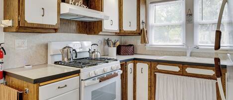 A kitchen with wooden cabinets, a stove, and a window with blinds.