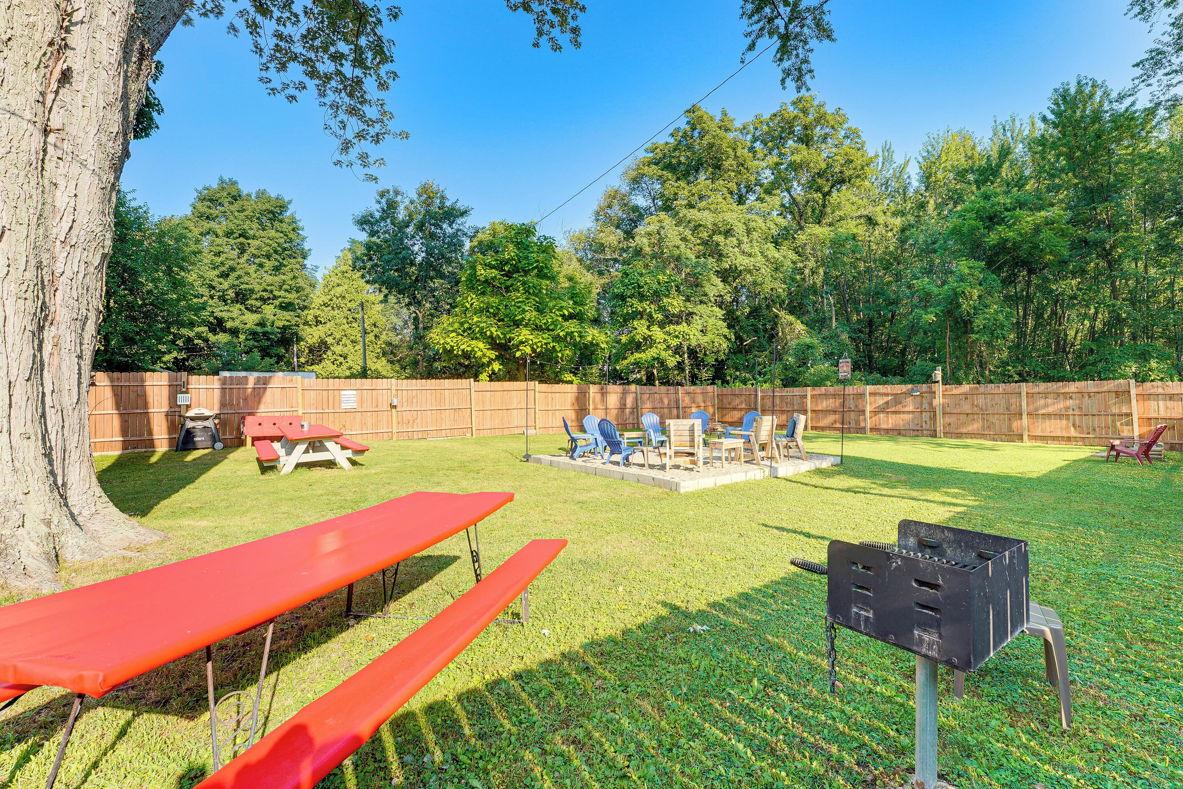 A backyard with picnic tables, a barbecue grill, and a wooden fence.