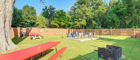 A backyard with picnic tables, a barbecue grill, and a wooden fence.