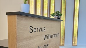A reception desk with multilingual welcome signage and a potted plant. - AMH - Wohnen auf Zeit (Munich)