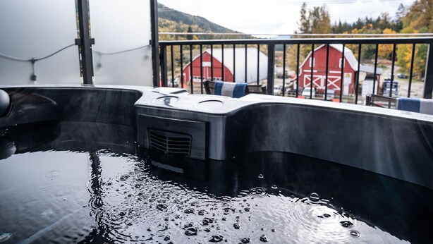 Un jacuzzi con vista a un granero rojo y montañas al fondo.