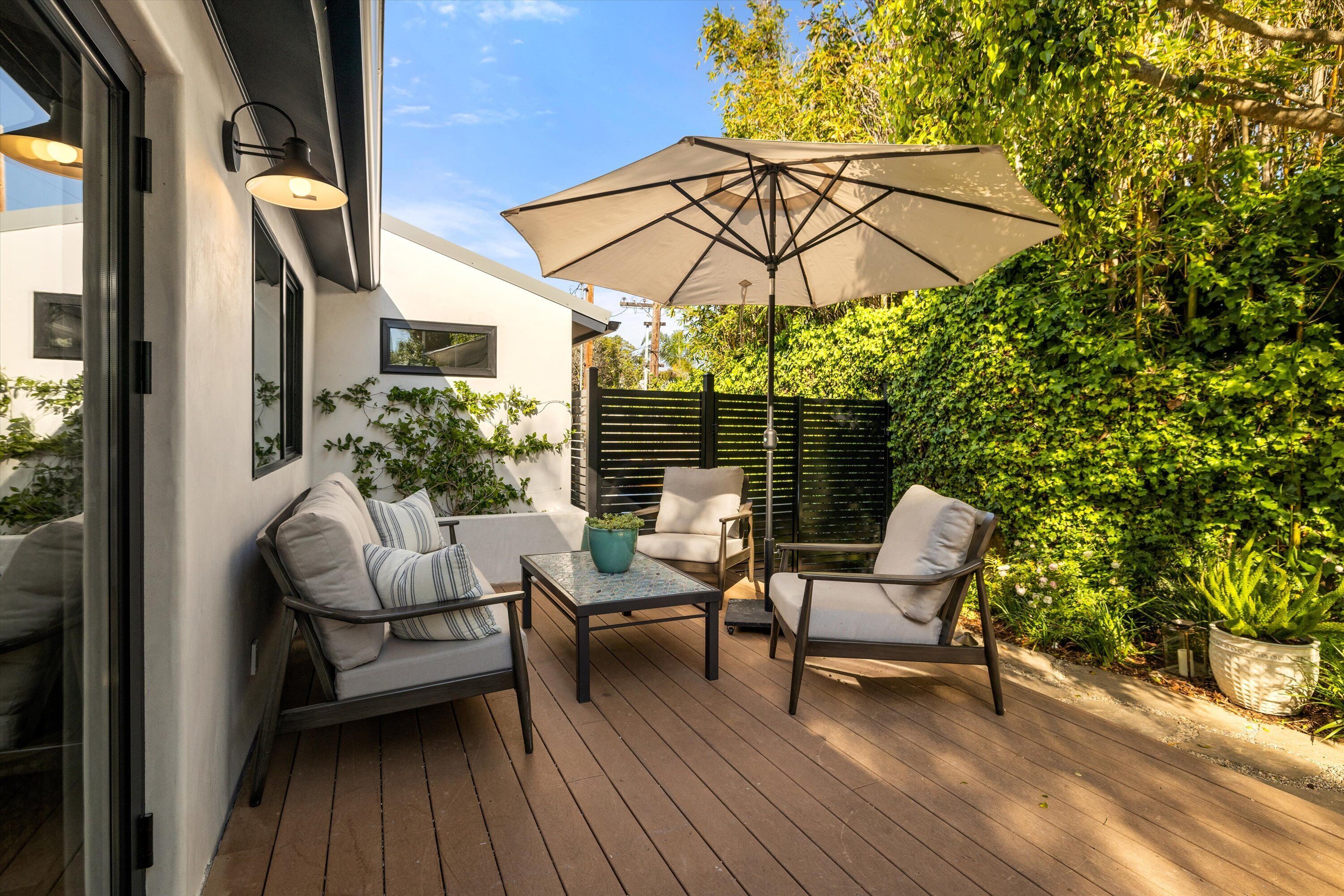 An outdoor patio with a wooden deck, two chairs, a table, and a large umbrella.
