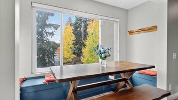 A dining area with a table and bench, a window with a view of trees, and a vase with flowers.