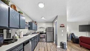 A modern kitchen with stainless steel appliances, a coffee machine, and a microwave. There is a red couch and a TV in the living area. - Snowy Peaks Haven | Walk to Slopes & Park (Brian Head)