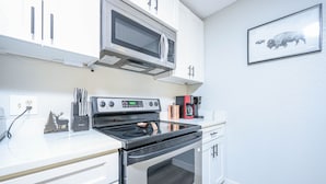 Una cocina con armarios blancos, un microondas de acero inoxidable, una estufa negra y un cuadro con la imagen de un búfalo en la pared.