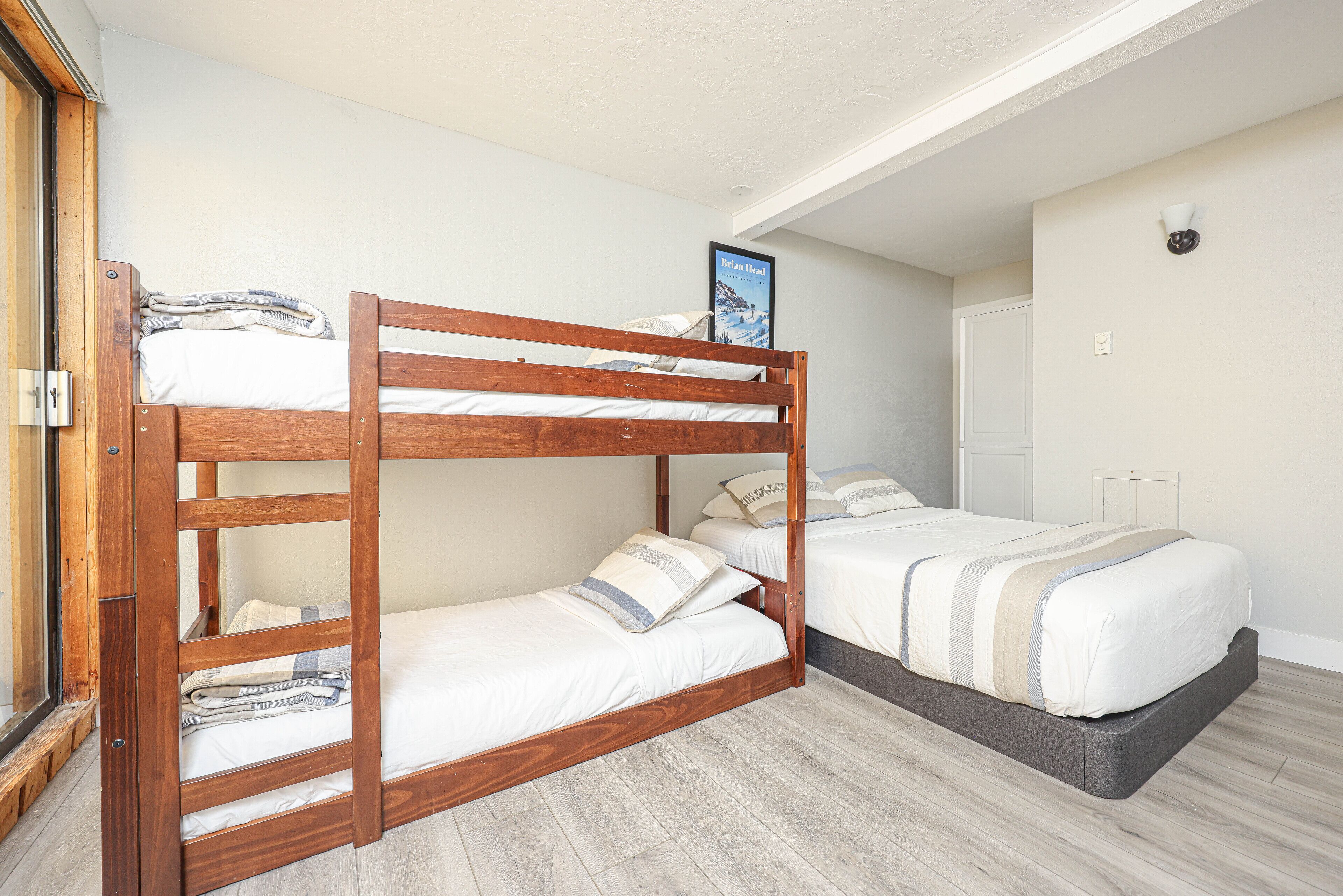A bunk bed room with a wooden frame, a lower bunk with a pillow, and a higher bunk with a pillow and a framed picture.
