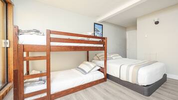 A bunk bed room with a wooden frame, a lower bunk with a pillow, and a higher bunk with a pillow and a framed picture.