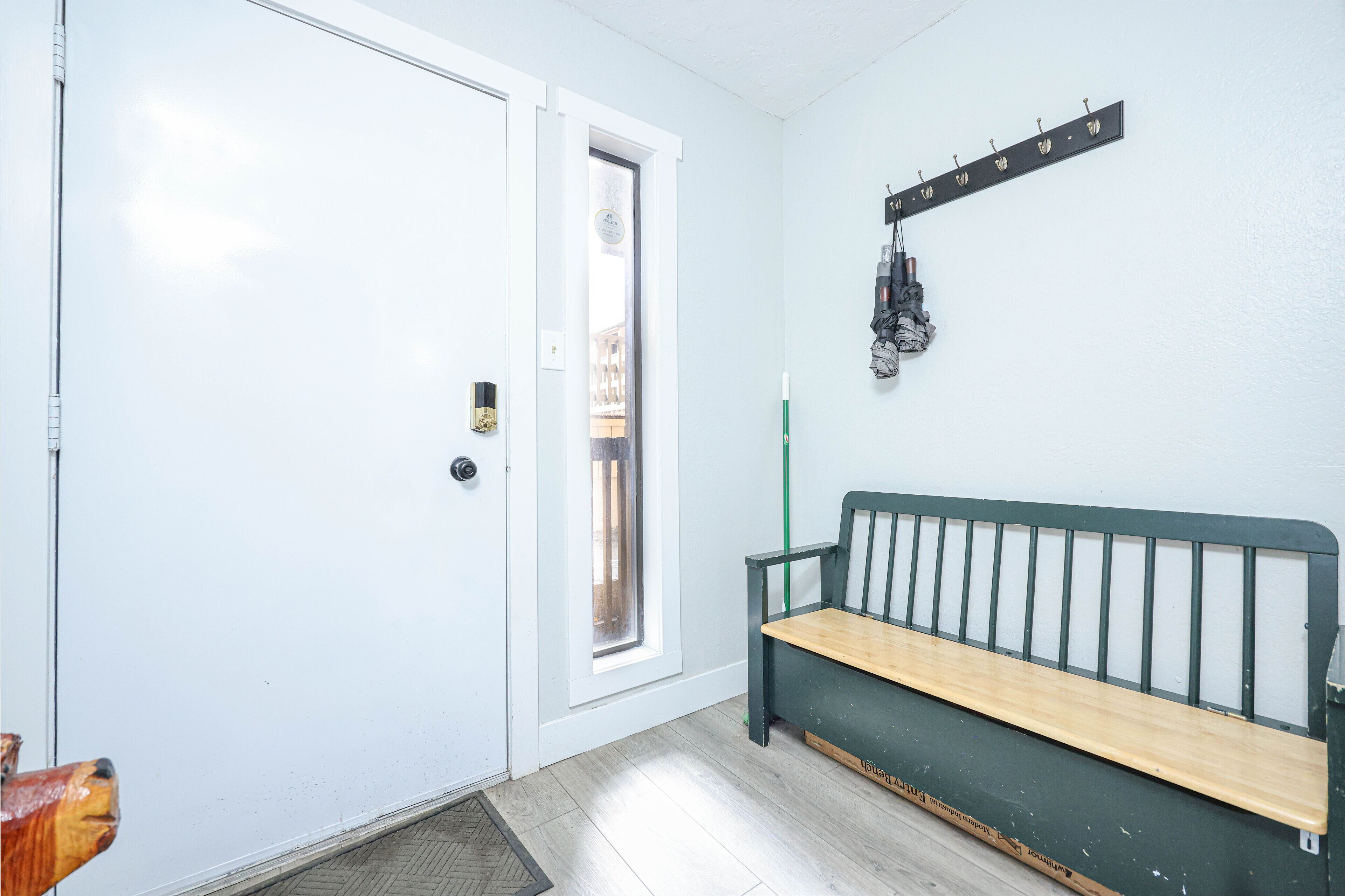 A room with a white door, a bench, a coat rack, and a window.