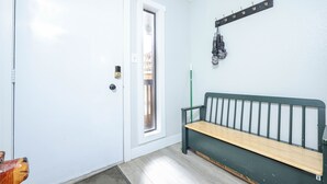 Una habitación con una puerta blanca, un banco, un perchero y una ventana.