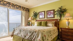 Ein Schlafzimmer mit einem großen Bett, einem Schminktisch, zwei Lampen und Blick ins Freie.