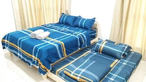 Una cama doble con colcha y almohadas a cuadros azules y amarillos, una toalla enrollada sobre la cama y un sillón-cama similar con el mismo diseño.