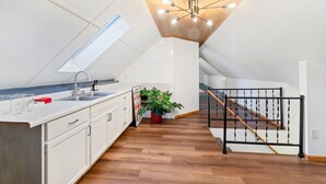 A modern kitchen with white cabinets, a wooden ceiling, and a black staircase railing. - Shuffleboard - Gym - BBQ (Minneapolis)