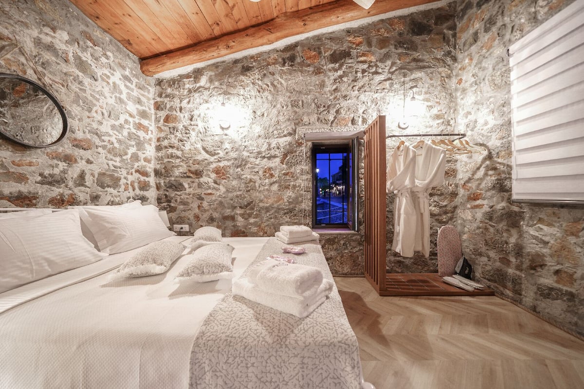 Een slaapkamer met stenen muren, een bed, handdoeken en een kledingrek voor jassen.