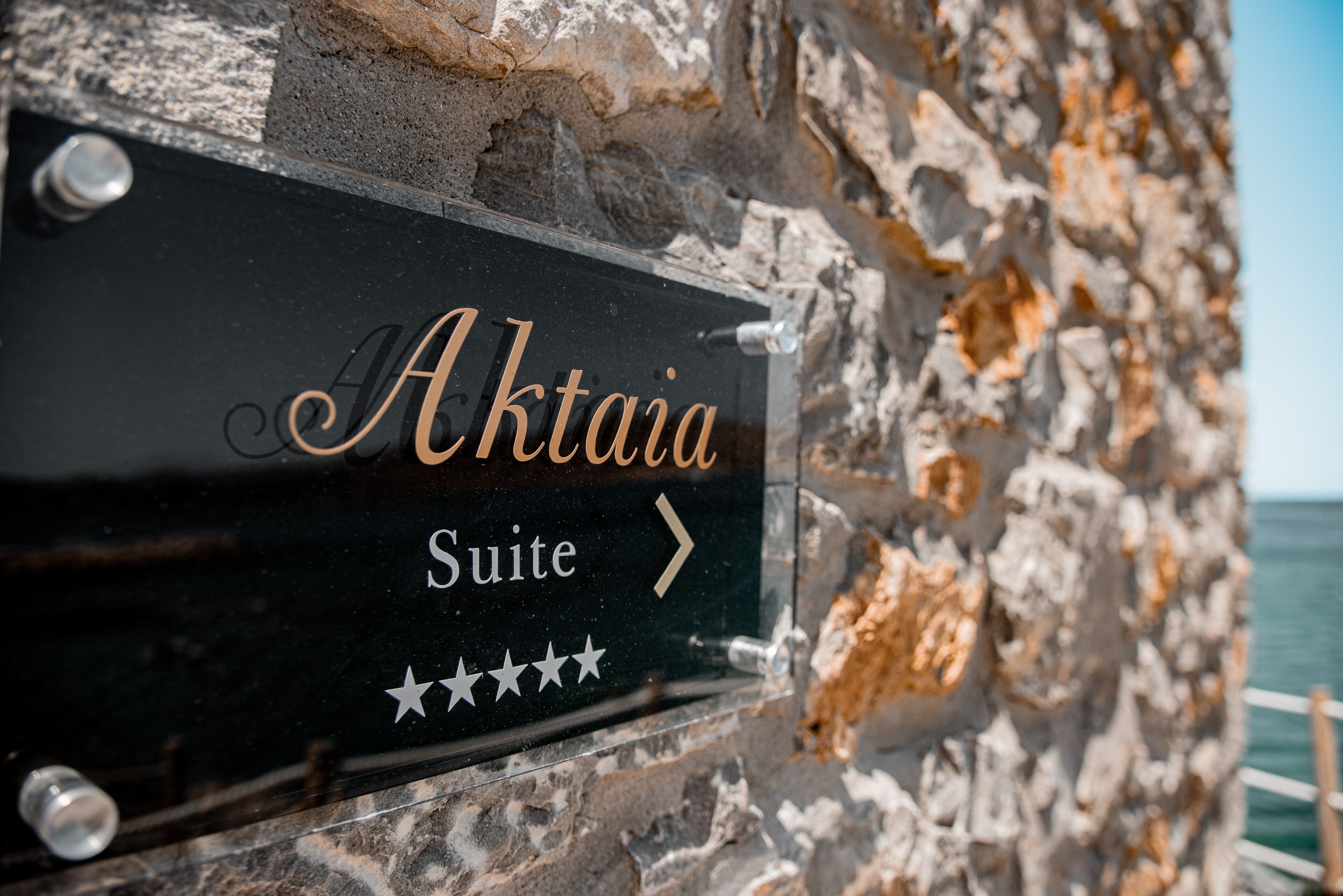 Señalización para "Aktaiia Suite" con una flecha indicando dirección, sobre un muro de piedra.