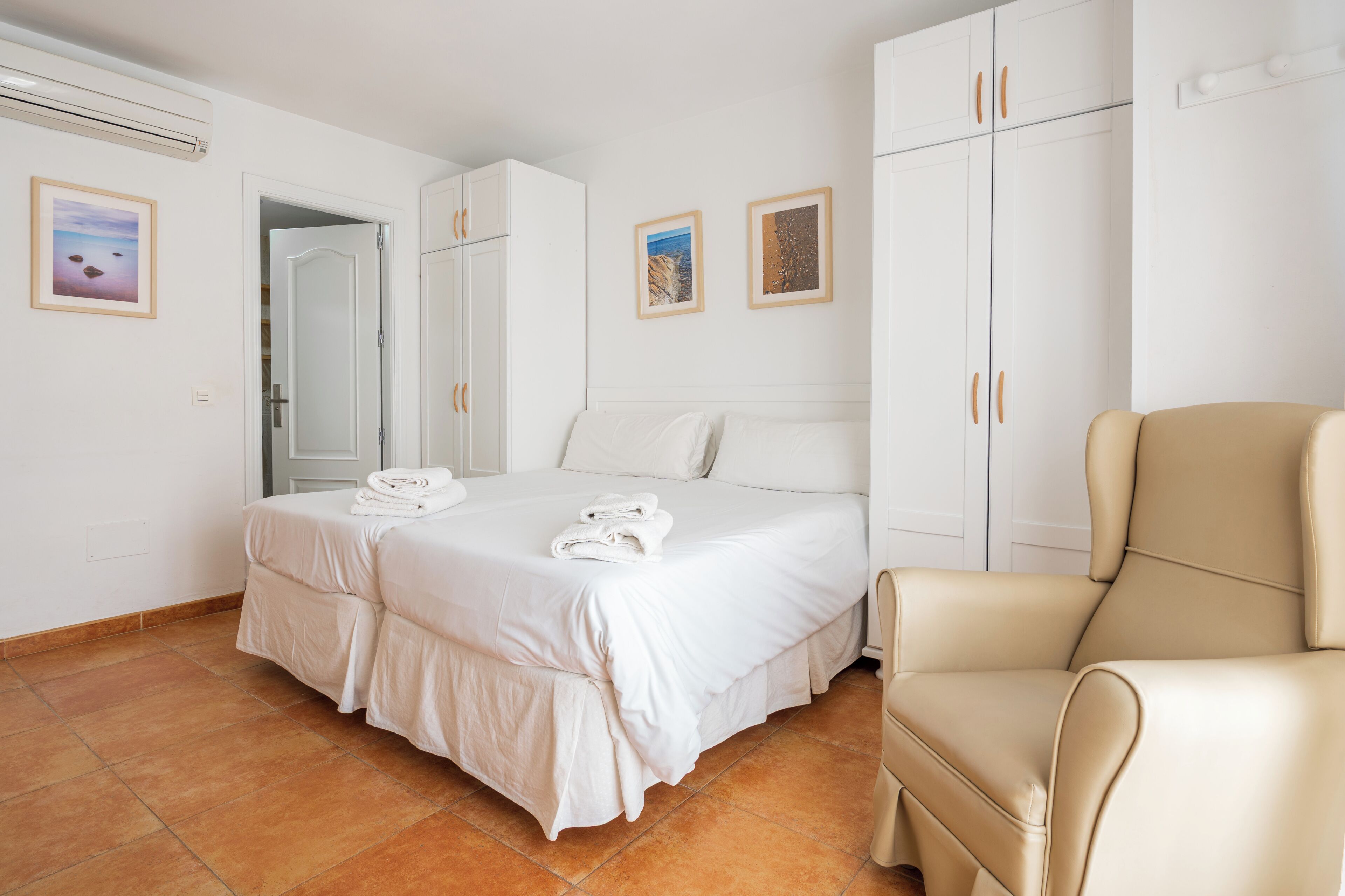 A bedroom with a bed, a chair, a wardrobe, and two framed pictures on the wall.