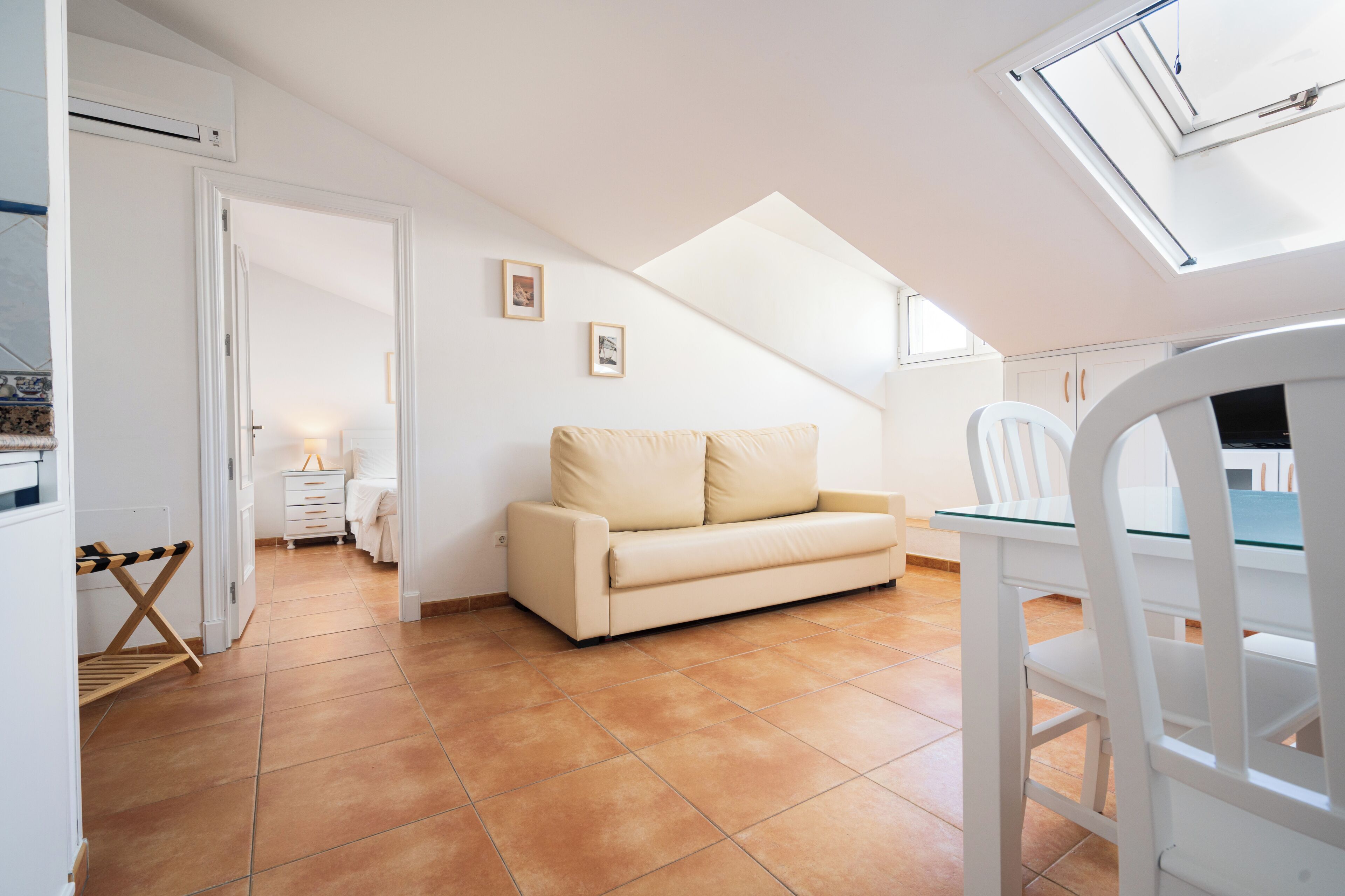 A modern apartment with a loft-style ceiling, a beige sofa, a dining table with chairs, and a small kitchen area.
