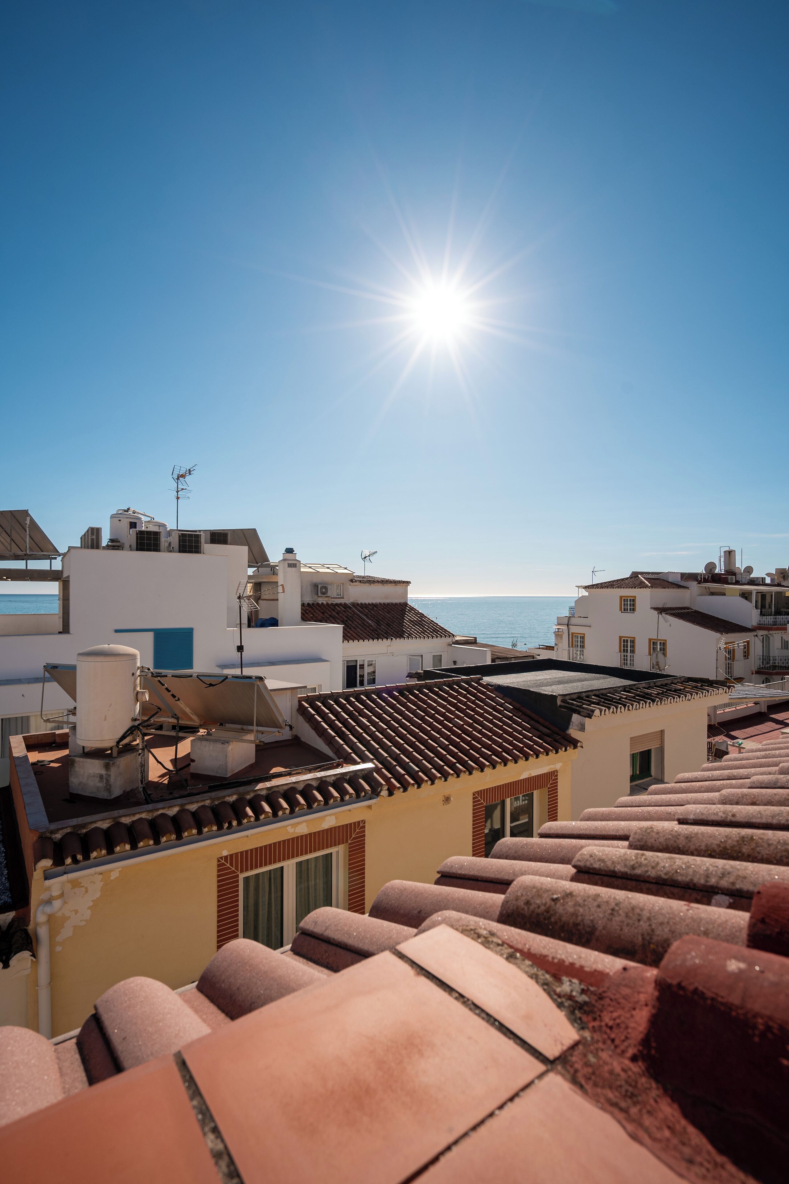 A rooftop with terracotta tiles, a clear sky, and buildings in the background.