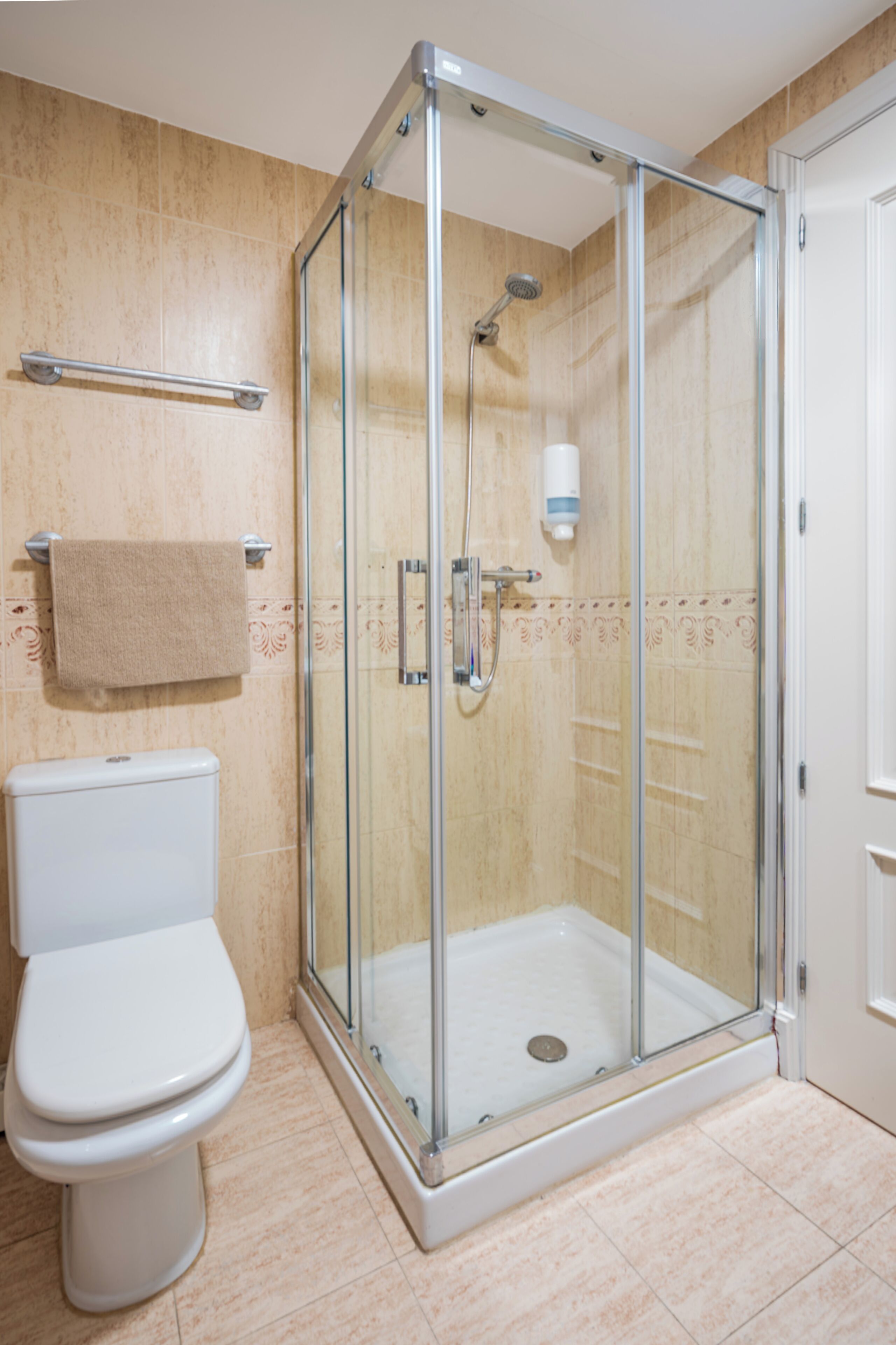Een badkamer met een douchecabine van glas, een wit toilet en een handdoekhouder.