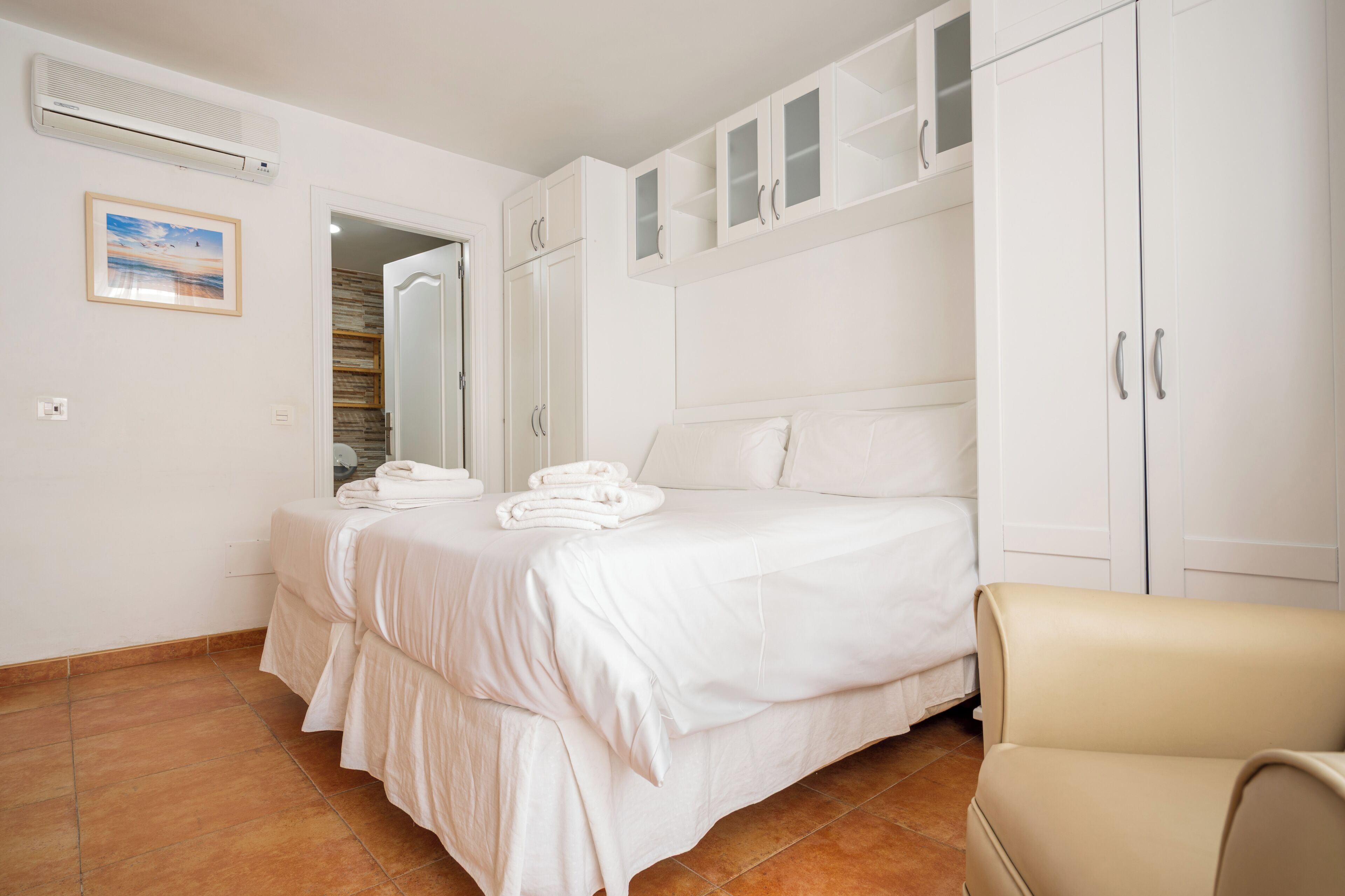 A bedroom with a bed, white wardrobe, and a chair.