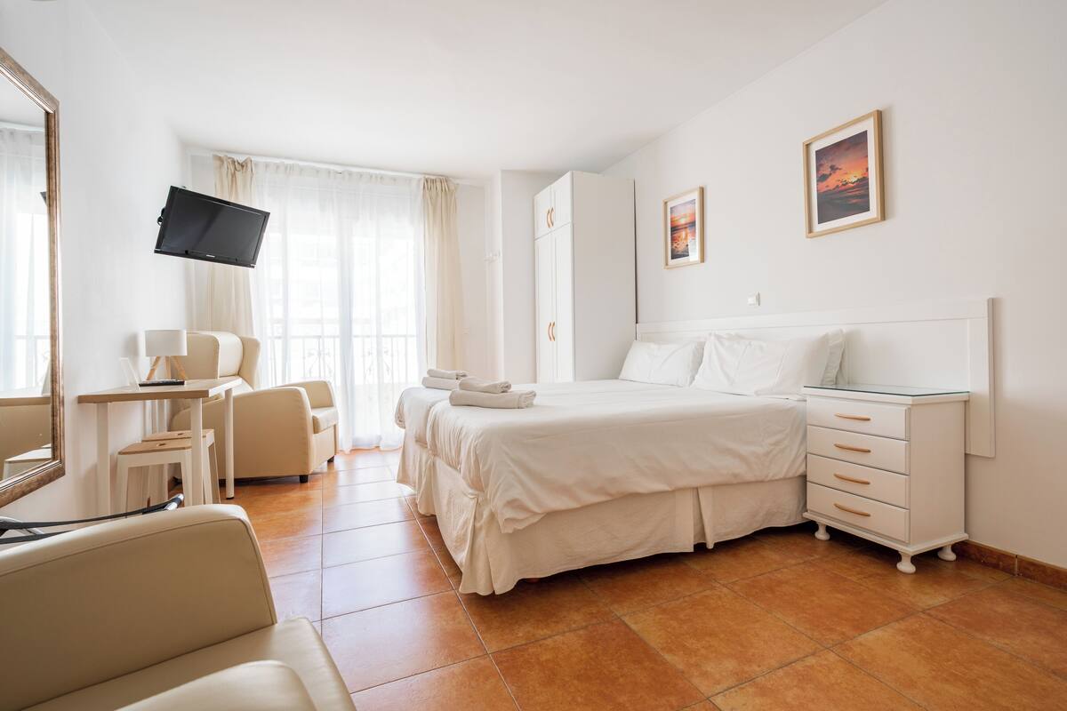 Una habitación de hotel con una cama, un escritorio con una silla, un televisor y un armario.