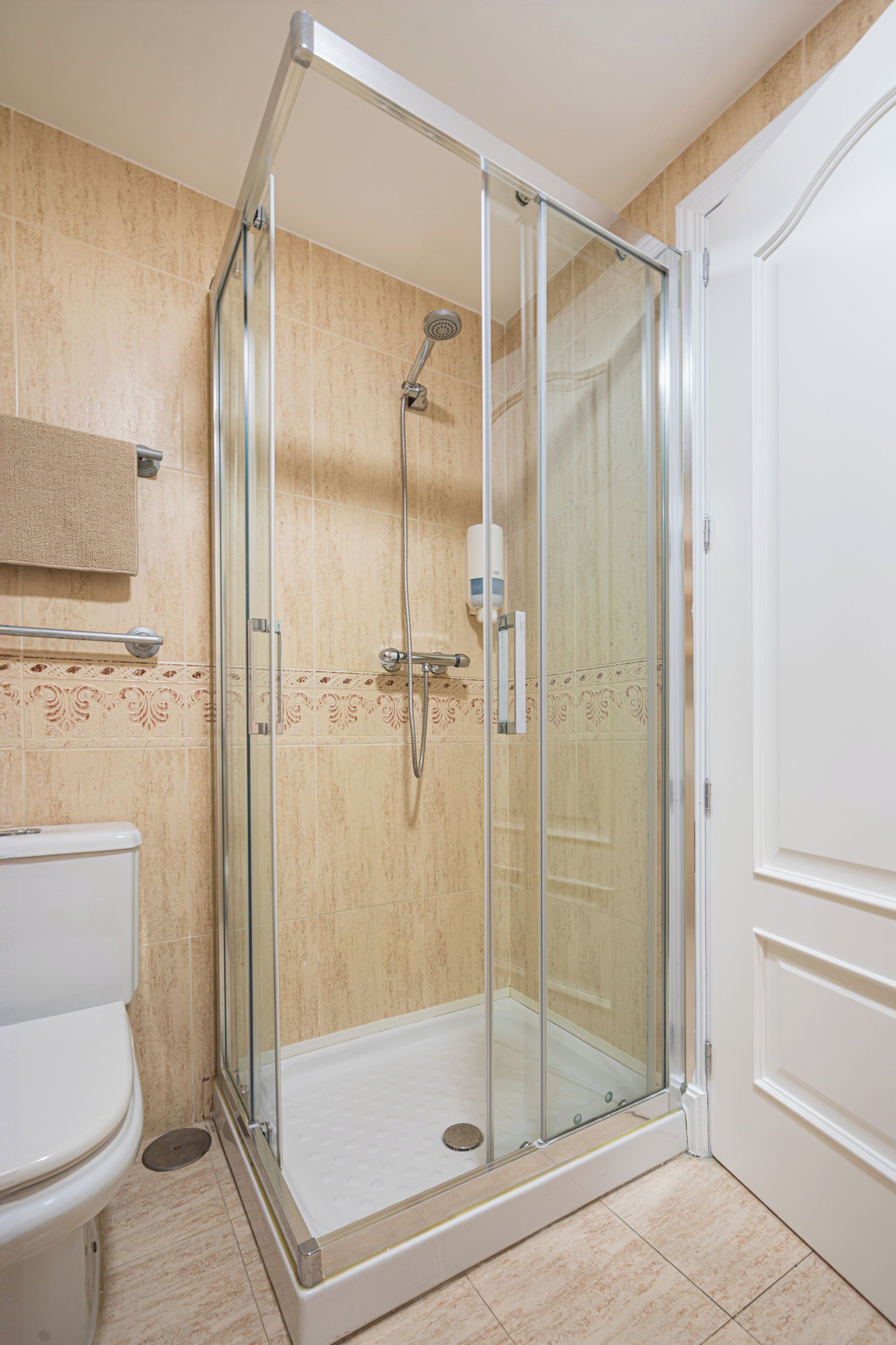 A glass-enclosed shower area with a white toilet and a towel rack.