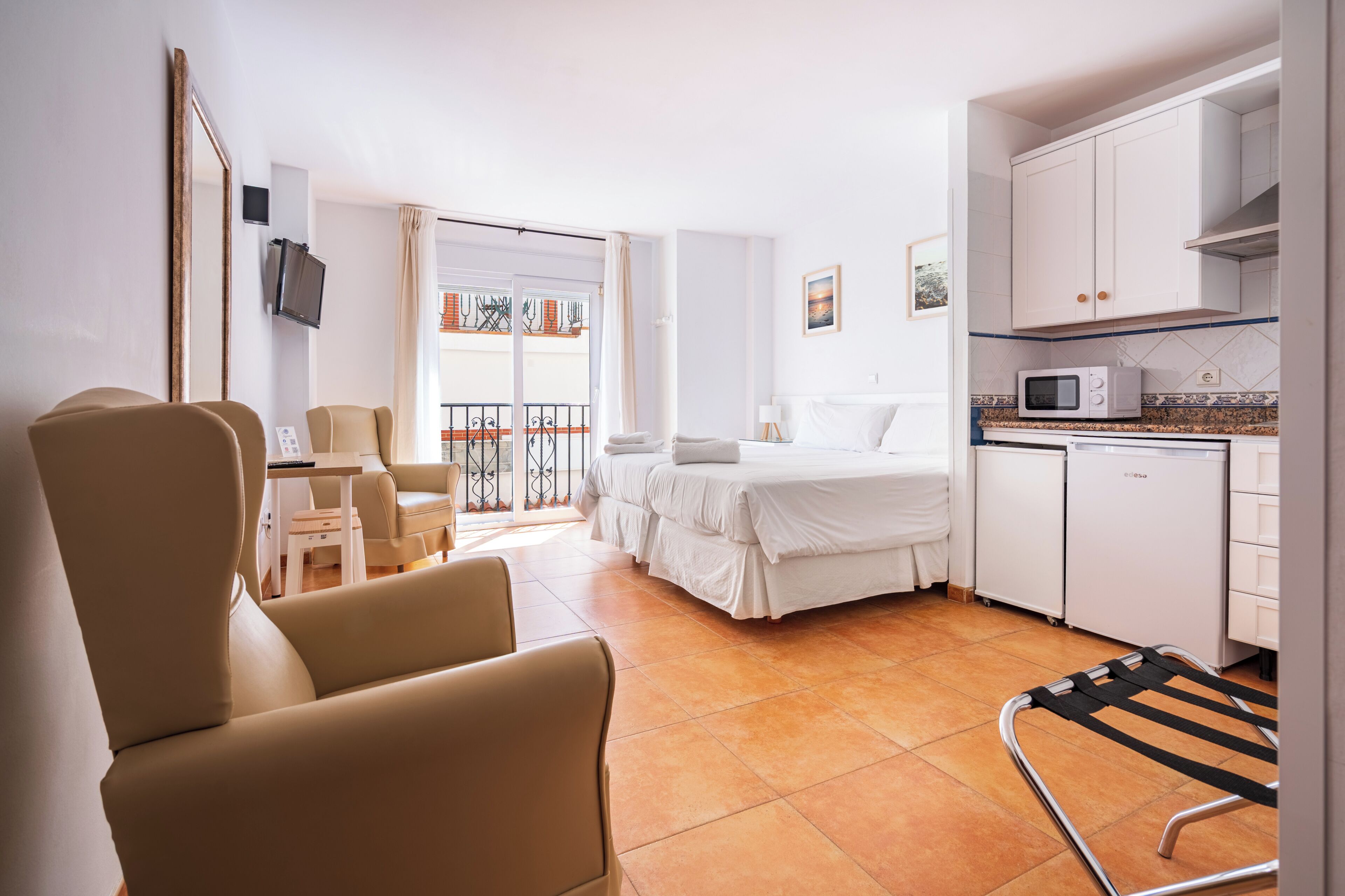 Ein Hotelzimmer mit Bett, Schreibtisch, Stuhl, Fernseher, einem Balkon mit Blick und einer Küchenzeile.