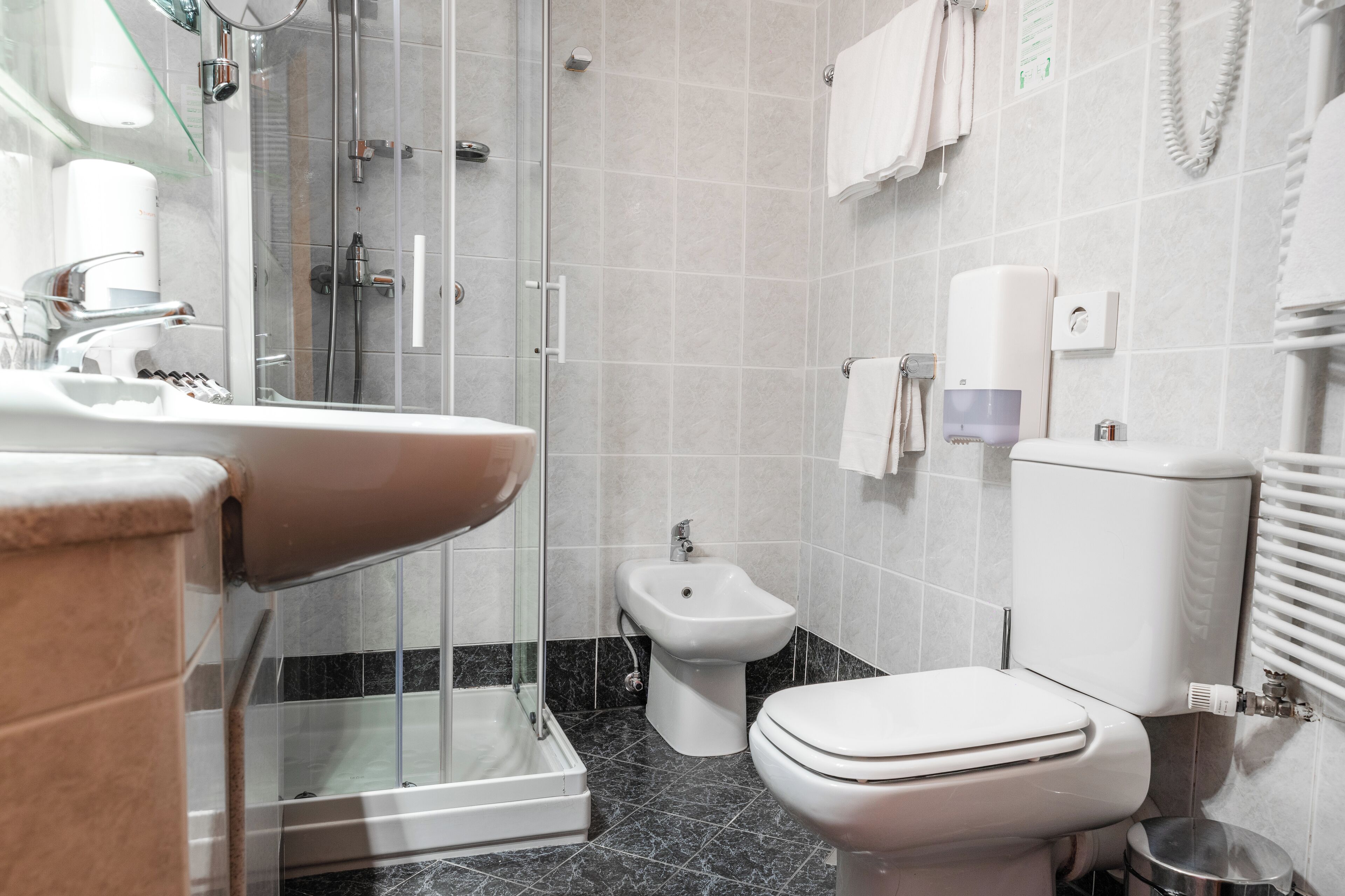 A modern bathroom with a glass-enclosed shower, a bidet, a toilet, and a sink.