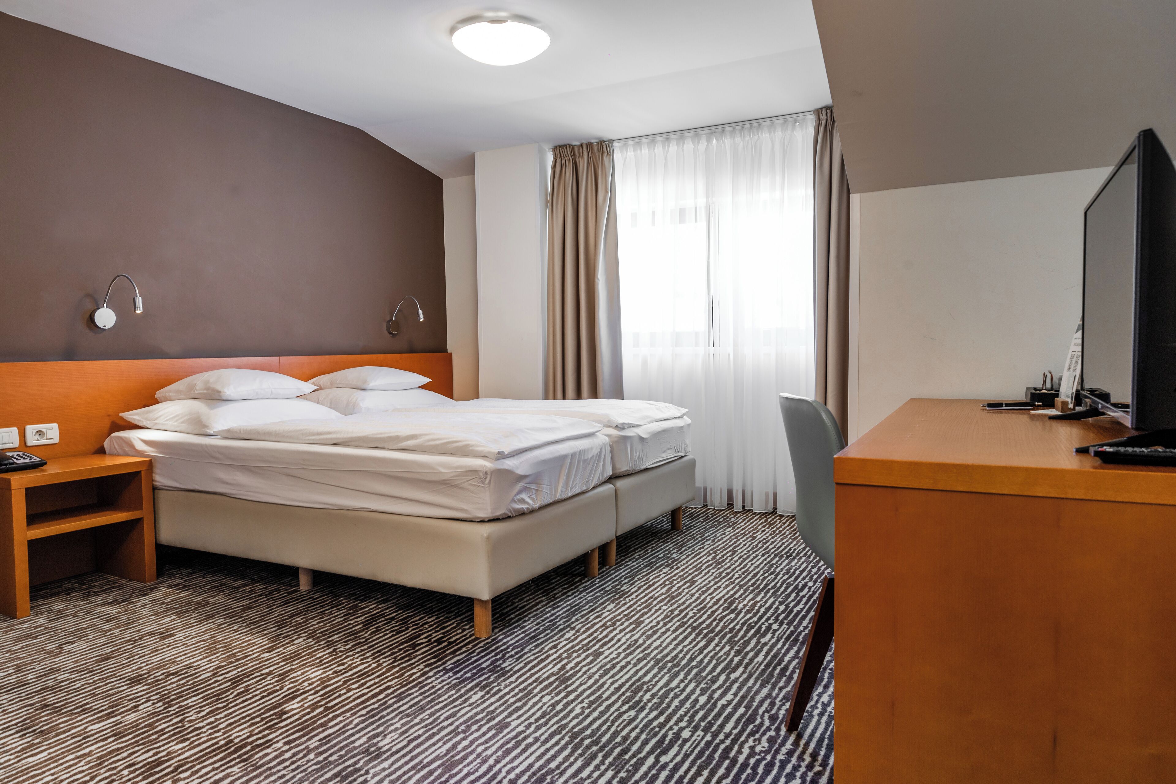 Een hotelkamer met een bed, nachtkastje, televisie en bureau.