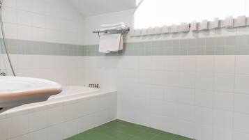 A bathroom with a white sink, green-tiled floor, white walls, a white bathtub, and a towel rack with folded towels.