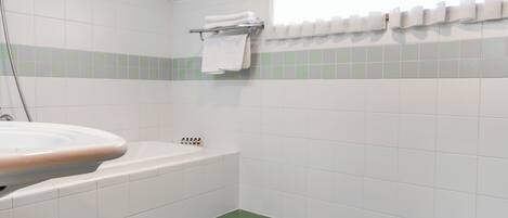 Un baño con lavamanos blanco, suelo con azulejos verdes, paredes blancas, bañera blanca y toallero con toallas dobladas.