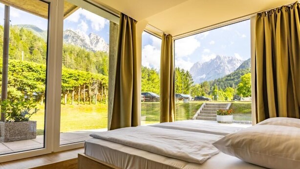 A bedroom with a large window offering a mountain view, a bed with white bedding, and a wooden headboard.