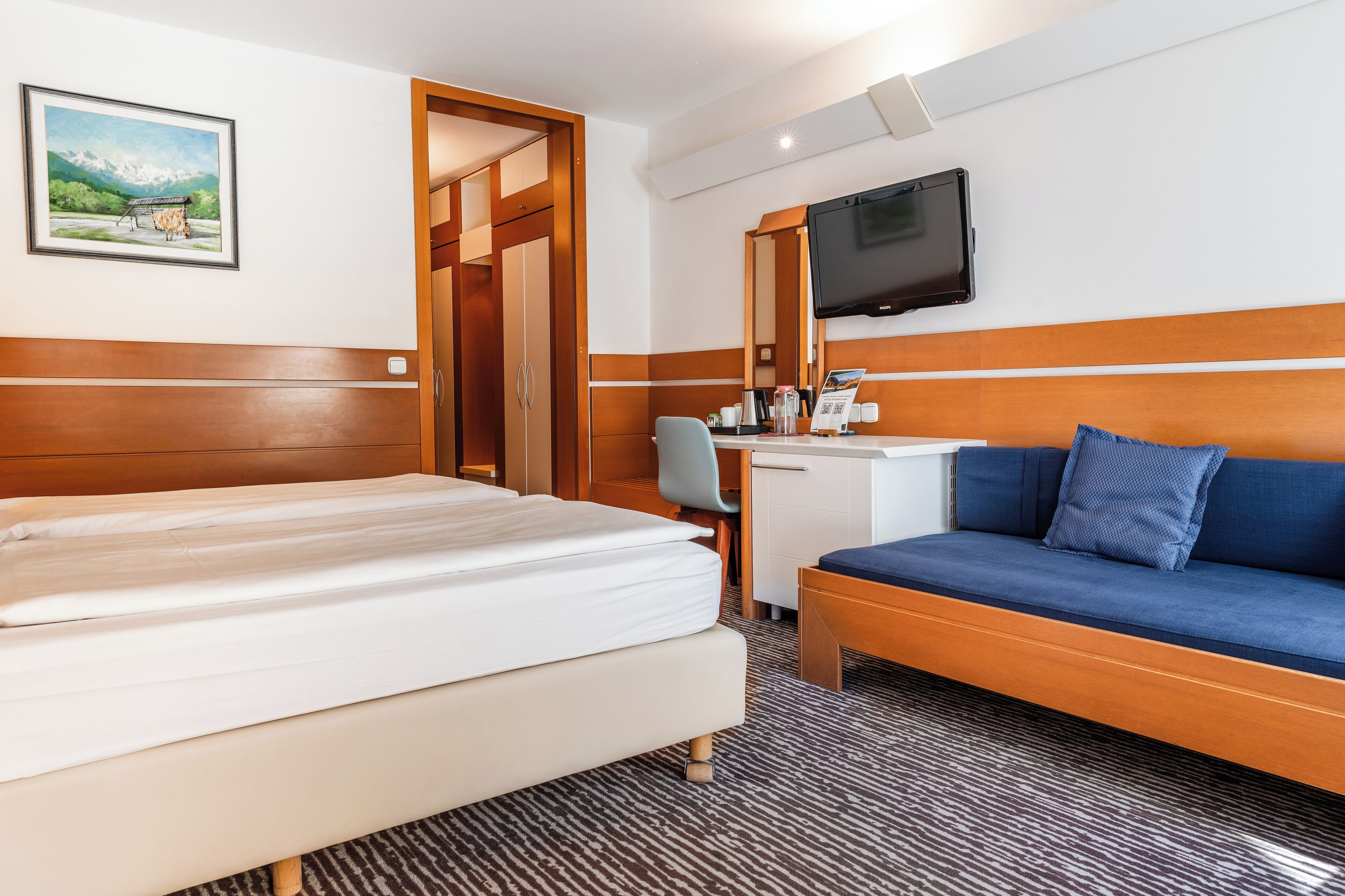 Une chambre d’hôtel avec un lit, un bureau, un canapé, une télévision et un tableau au mur.