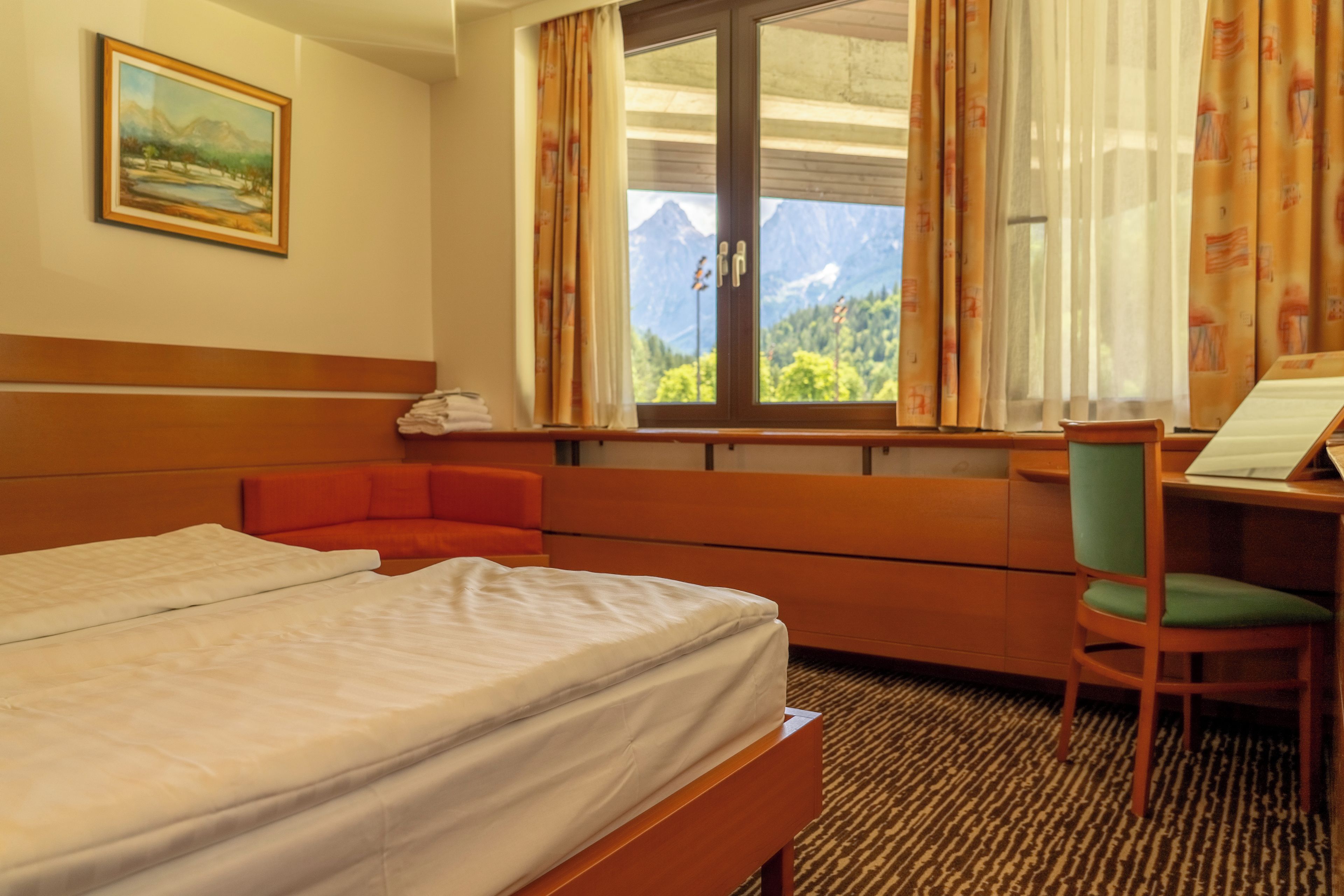 Habitación de hotel con cama, escritorio, silla y ventana con vista a la montaña.