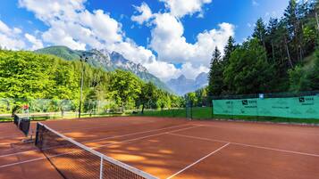 Un court de tennis avec un filet, entouré d’une végétation luxuriante et avec des montagnes en arrière-plan.
