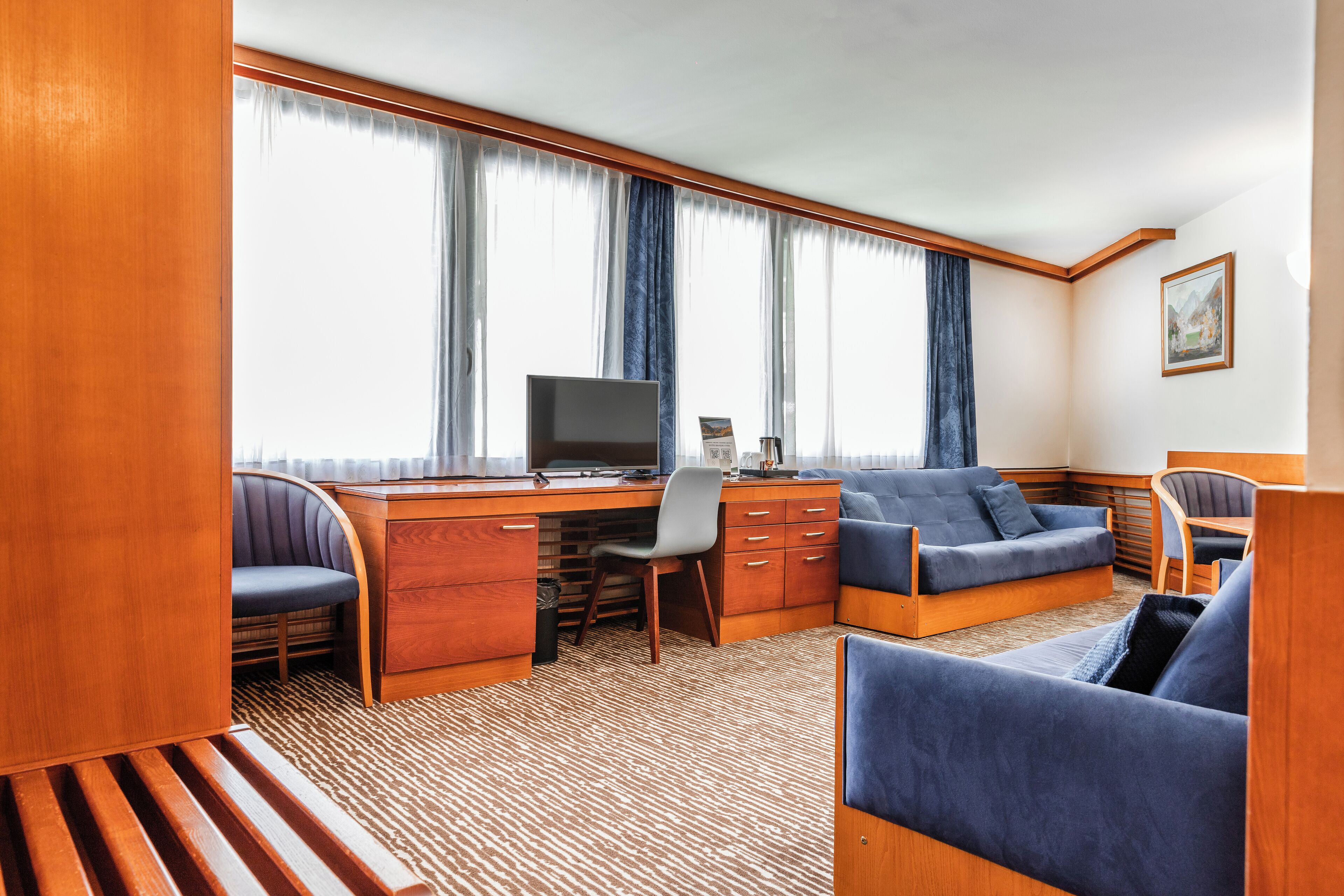 Une pièce compacte et bien éclairée, avec un bureau en bois, un ordinateur, un canapé bleu et une chaise.