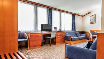 A compact, well-lit room with a wooden desk, a computer, a blue sofa, and a chair.