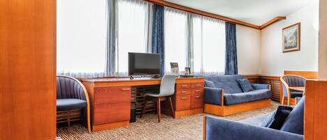 Une pièce compacte et bien éclairée, avec un bureau en bois, un ordinateur, un canapé bleu et une chaise.