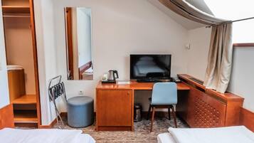 Quarto de hotel com uma cama, uma escrivaninha, uma cadeira, uma televisão e um guarda-roupa.