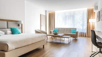 A hotel room with a bed, a sofa, a desk, and a large window with curtains.