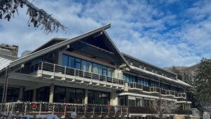 A modern hotel with multiple balconies, large windows, and a ski slope in the background.