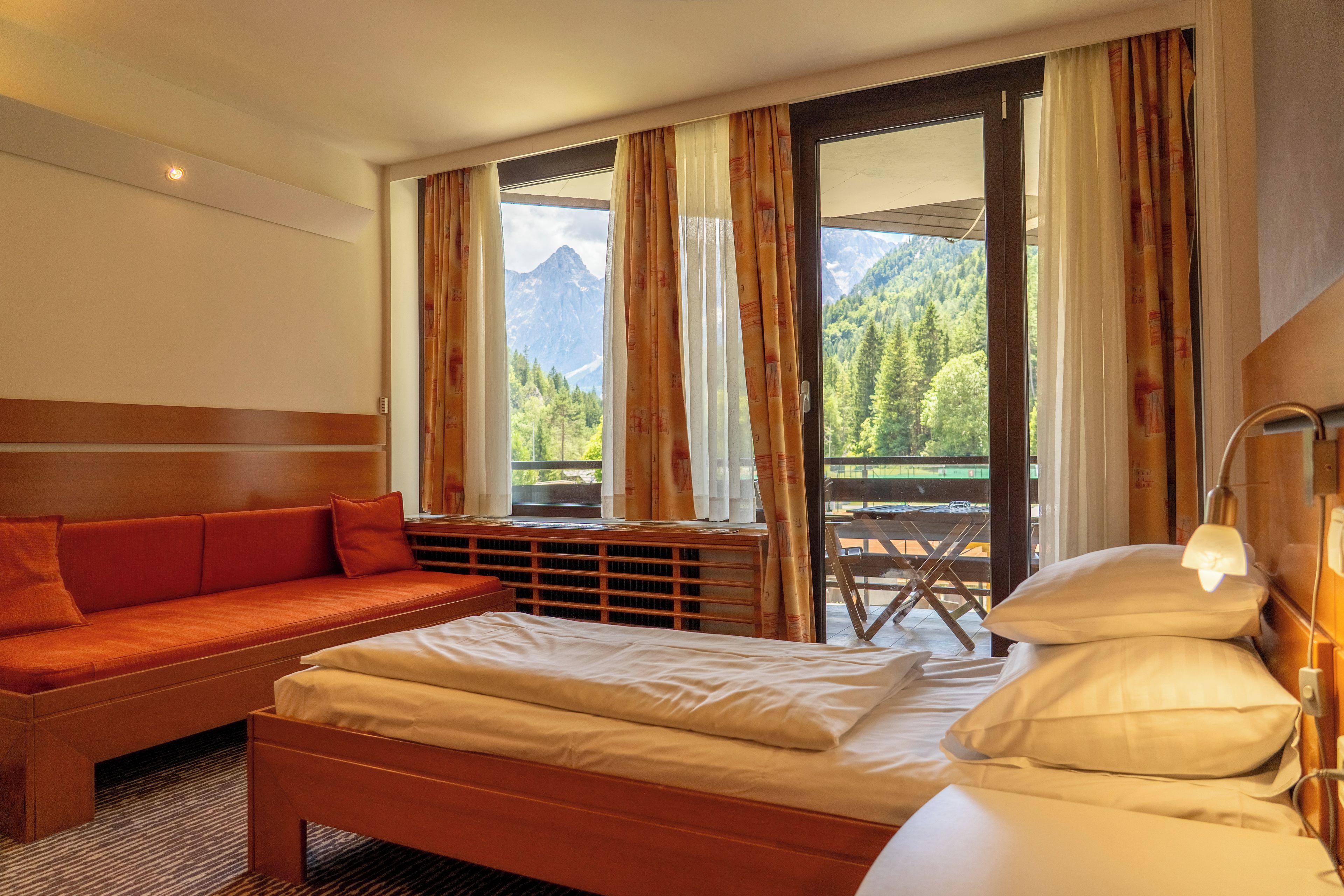 A hotel room with a bed, a sofa, a desk, and a view of mountains through the window.