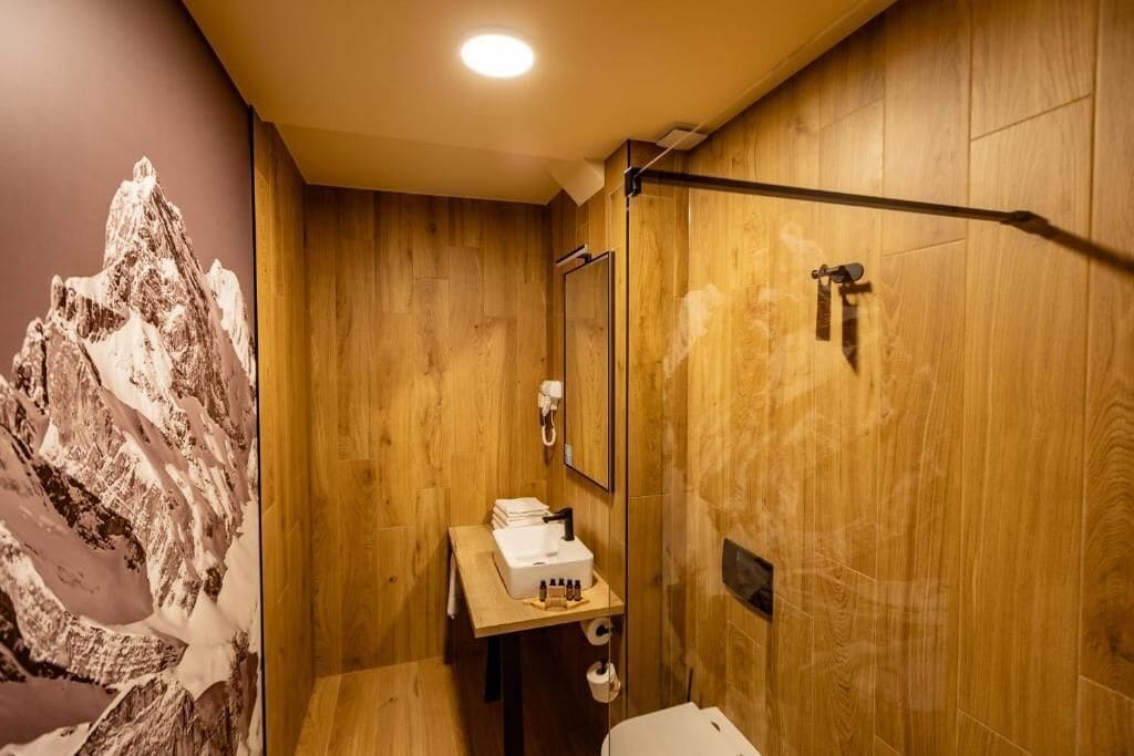 A wooden bathroom with a sink, mirror, and shower.